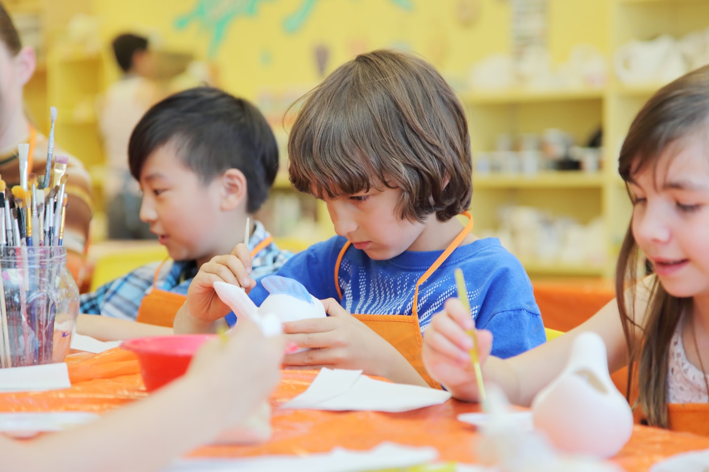 Children painting ceramic figures at a messy art table