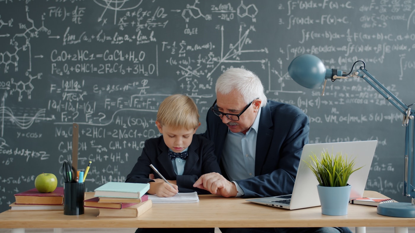 Teacher kneeling beside a young student at her desk